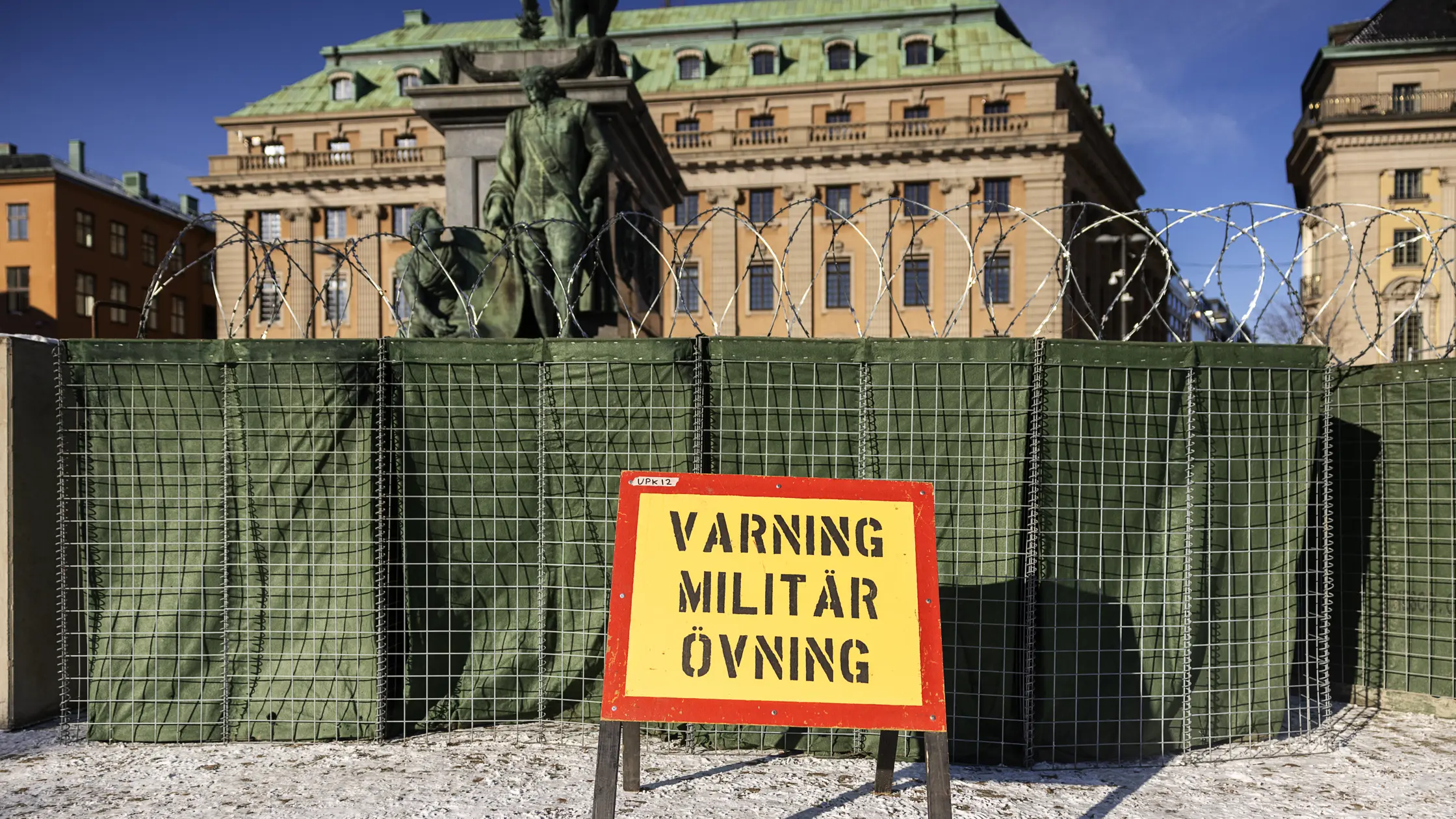En gul och röd skylt med texten "Varning militär övning". Bakom skylten ett avspärrat område i centrala Stockholm.