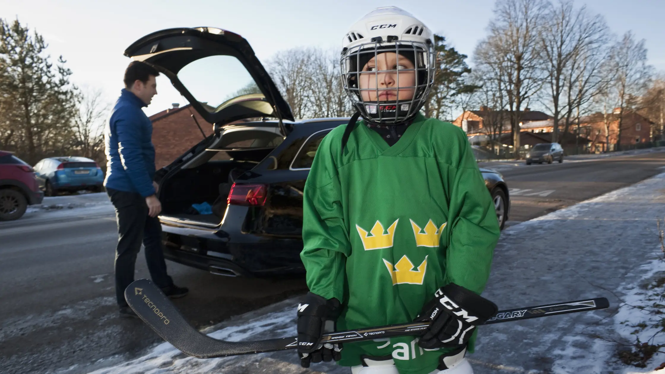 Pojke i hockeyutrustning väntar på en vuxen som packar bilden i bakgrunden.