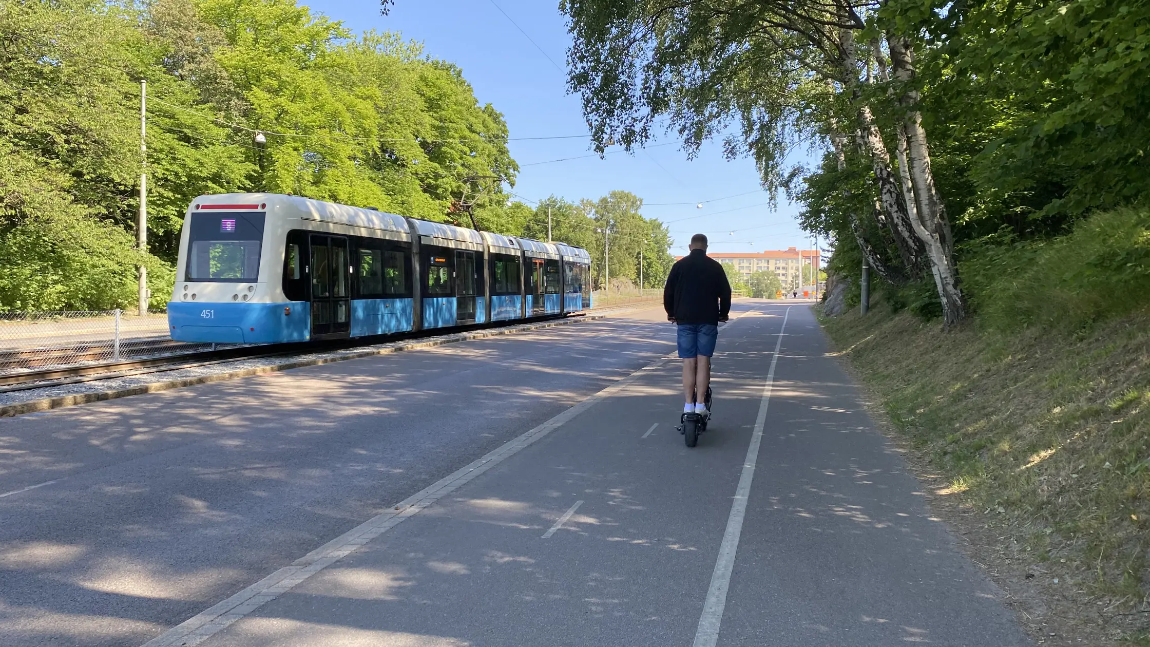 En spårvagn kommer åkandes och en man på en elsparcykel sussar förbi bredvid på en cykelbana. 