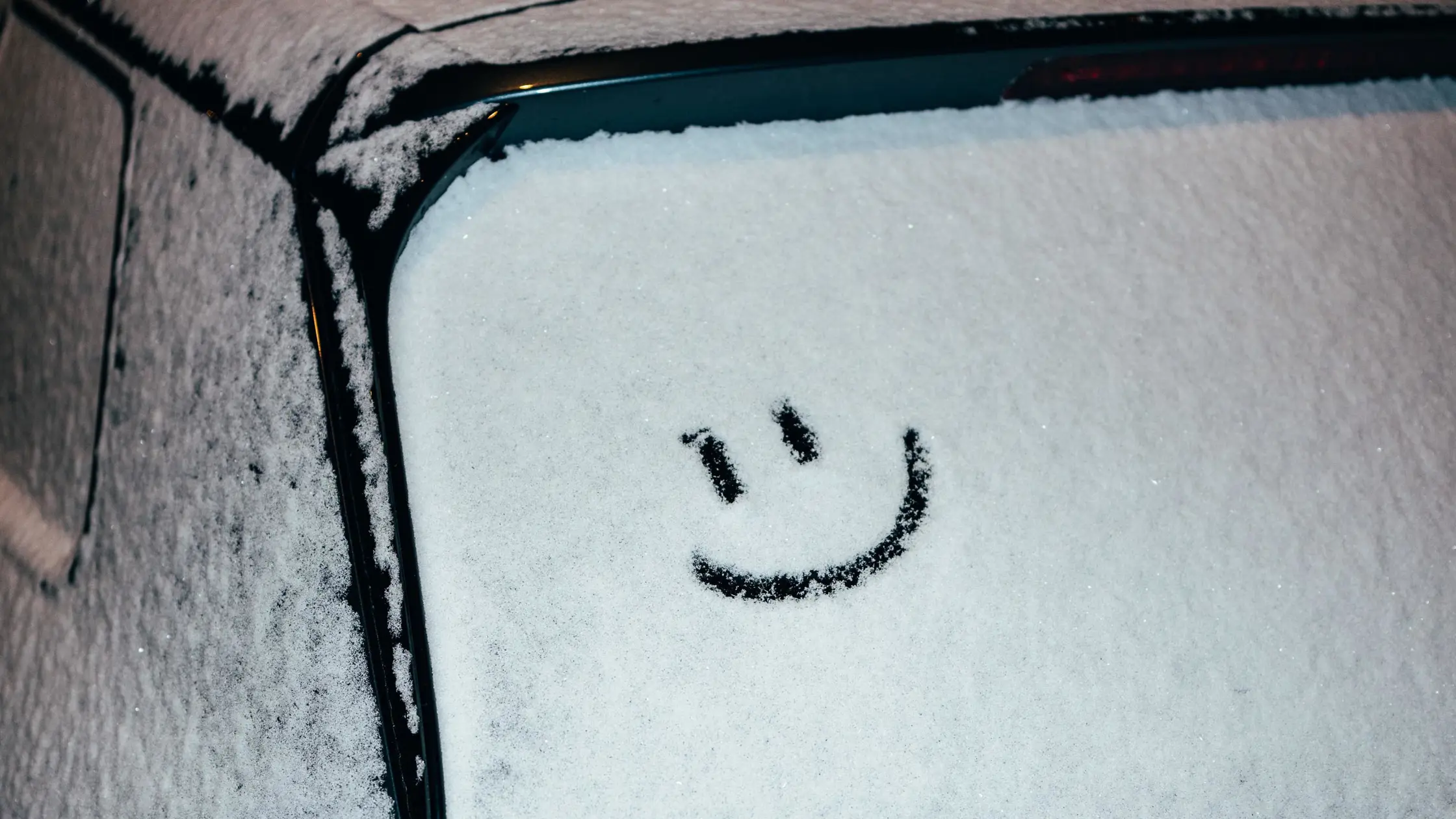 Någon har ritat en glad smiley i snön bak på en bil.