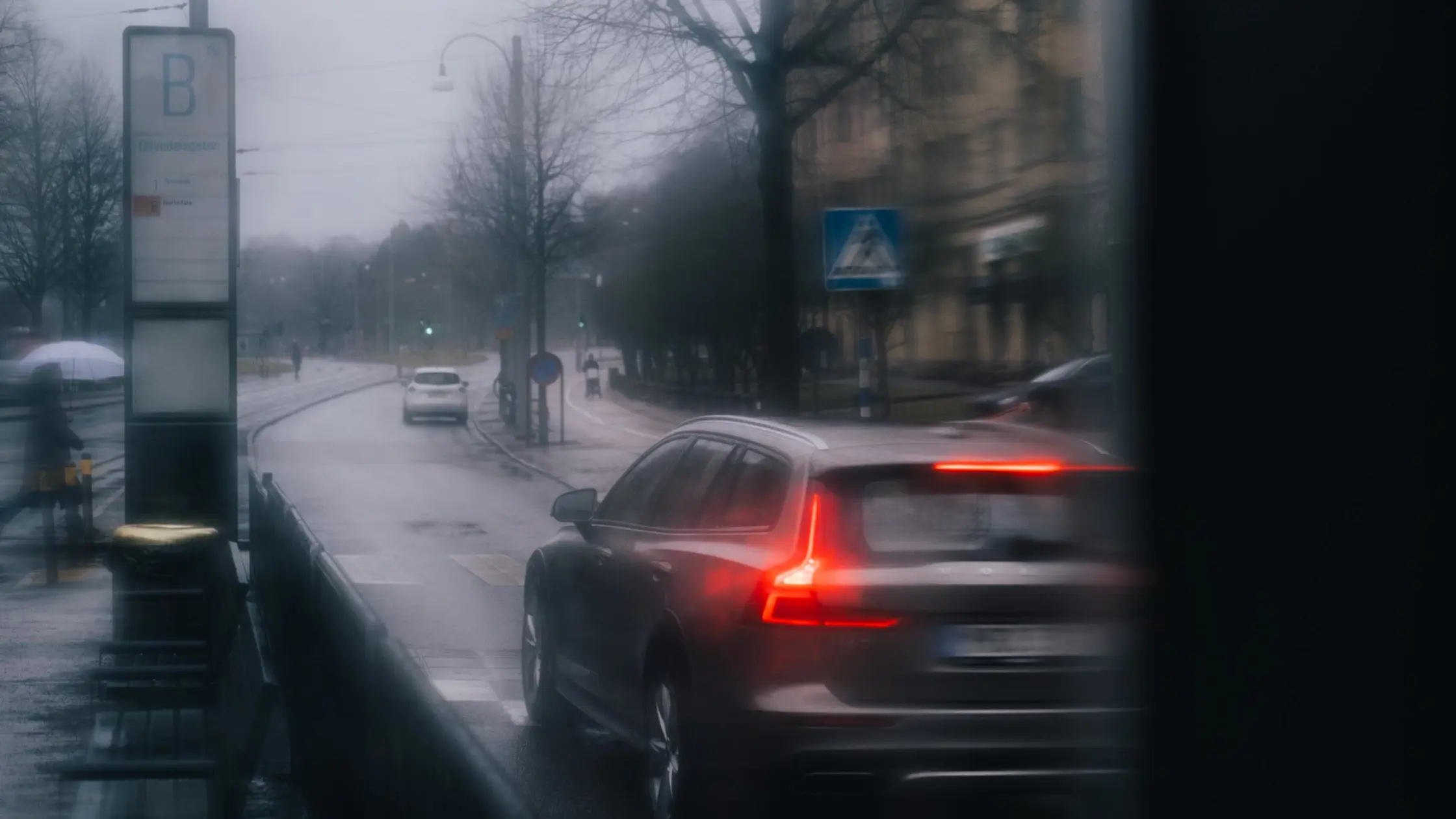 En personbil kör i regn och dålig sikt. En hållplats syns till vänster i bild.