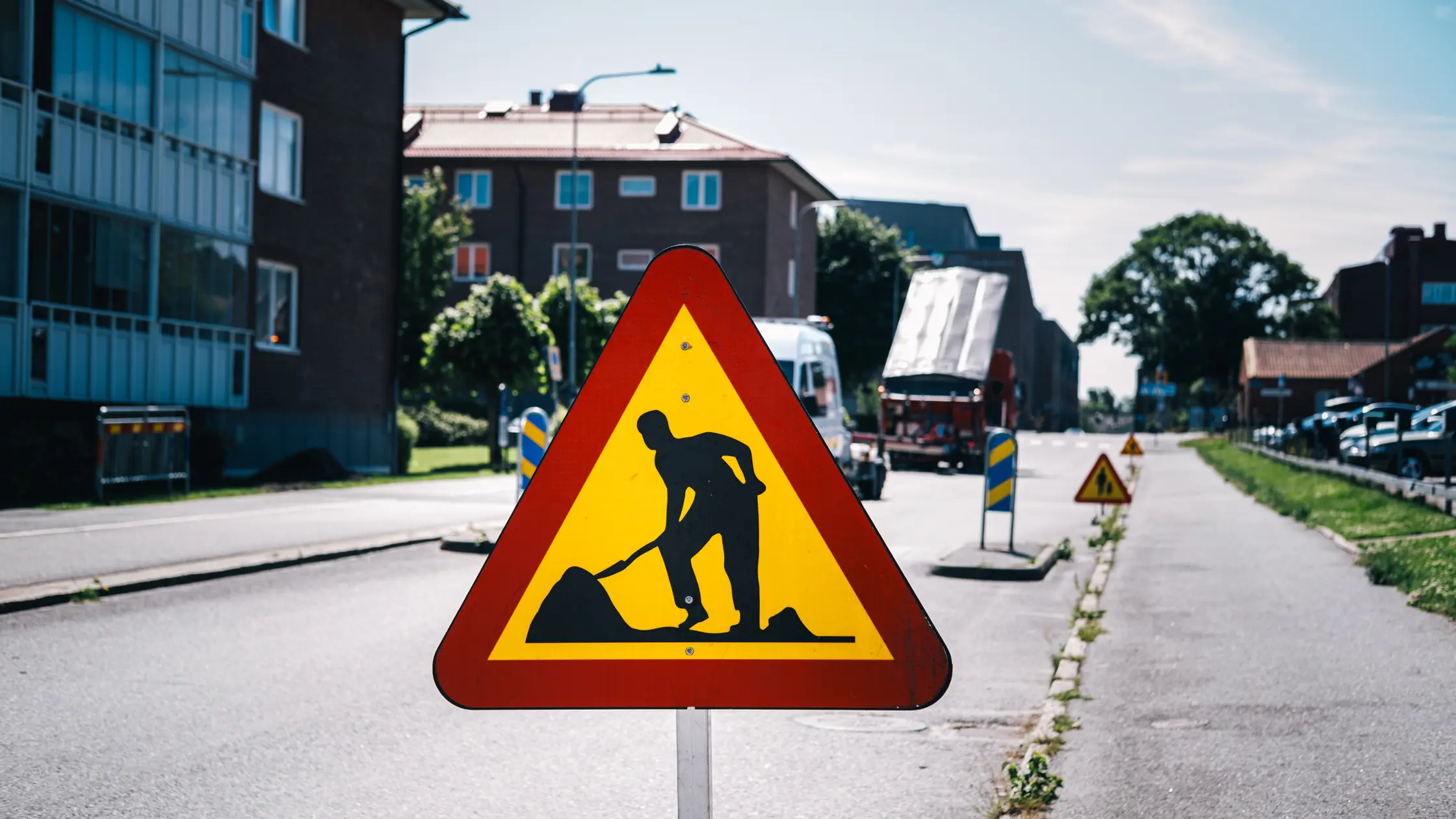 En vägarbetsskylt syns och fler skyltar syns i bakgrunden. Även byggnader till vänster i bild. 