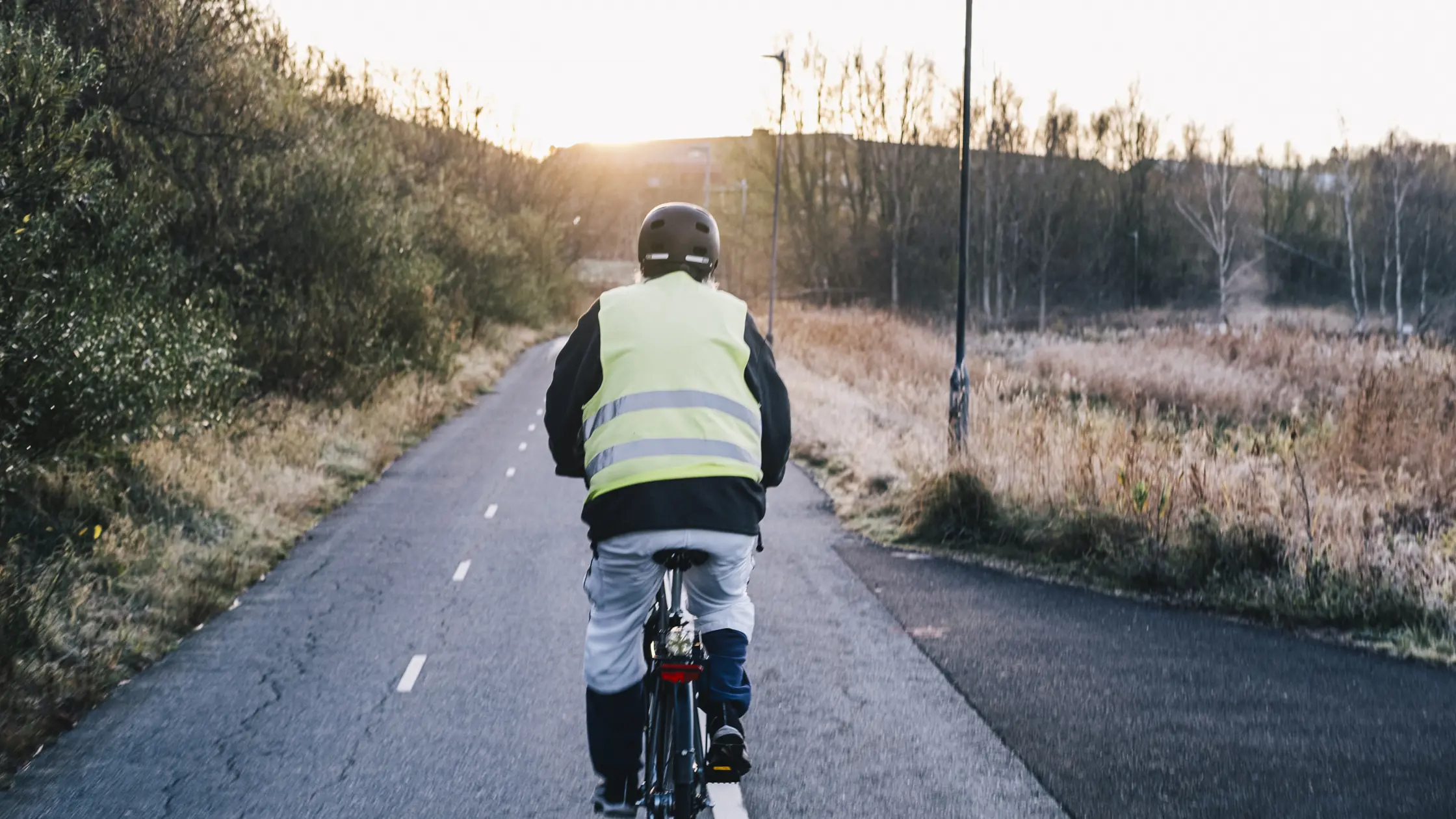 En cyklist syns bakifrån med en reflexväst och hjälm på sig.