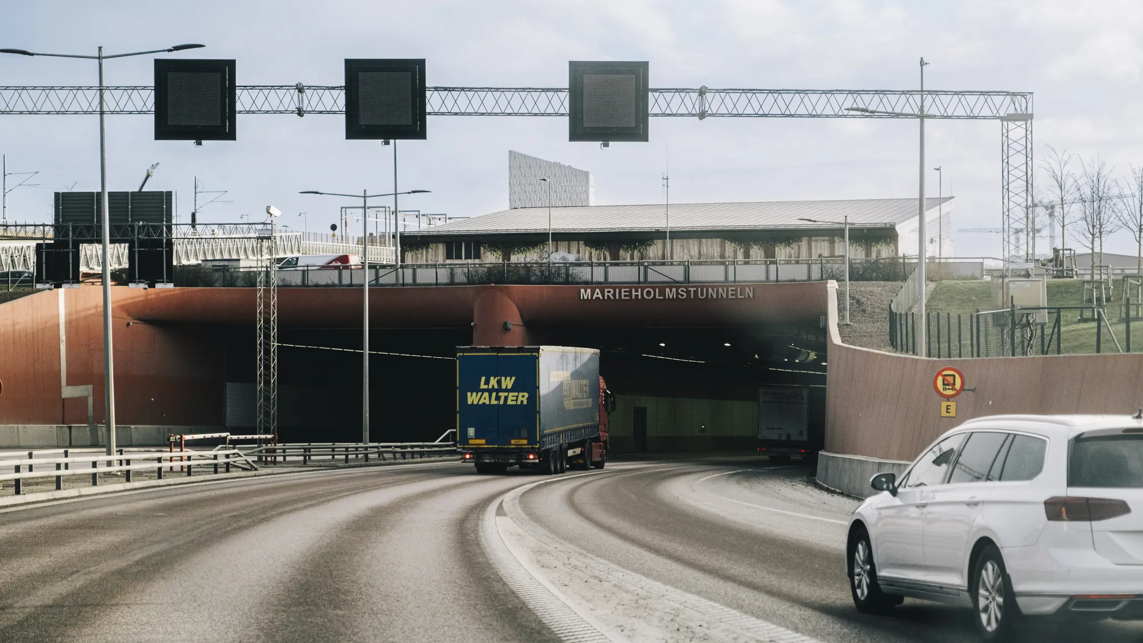 En lastbil och en personbil är på väg att köra in i Marieholmstunneln. Tunnelmynningen med skylt där det står Marieholmstunneln syns i bakgrunden.