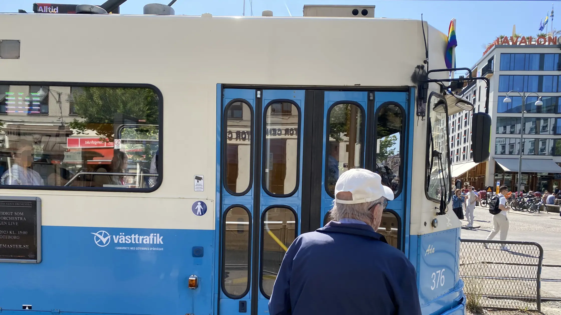 Spårvagn är stillastående vid hållplats Kungsportsplatsen. En äldre man väntar på perrongen med ryggen mot kameran. 