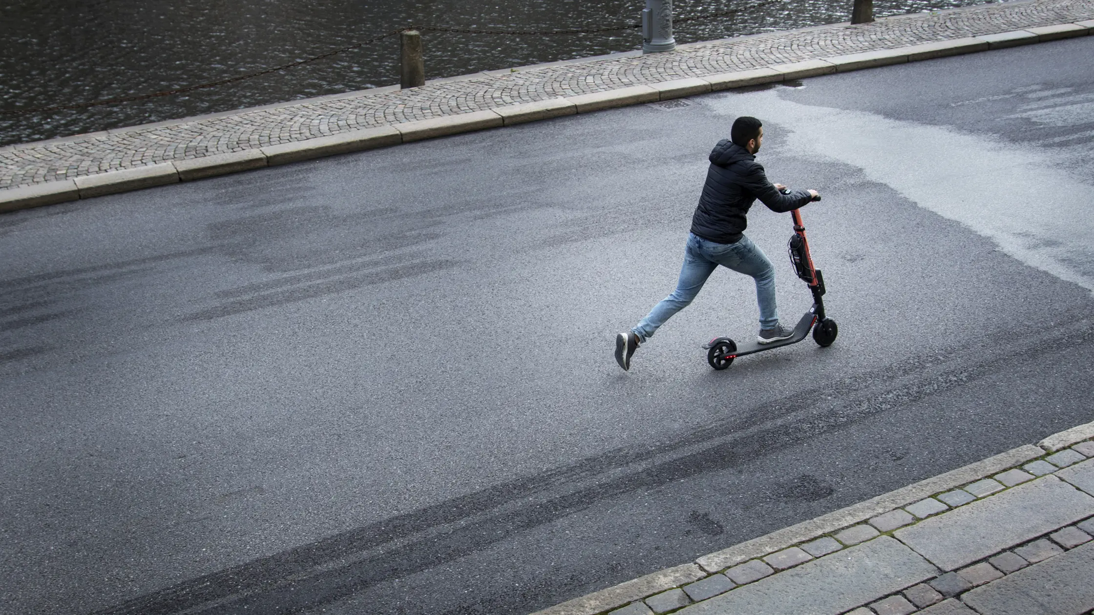 En man står med ena foten på en elsparkcykel och kör framåt. 