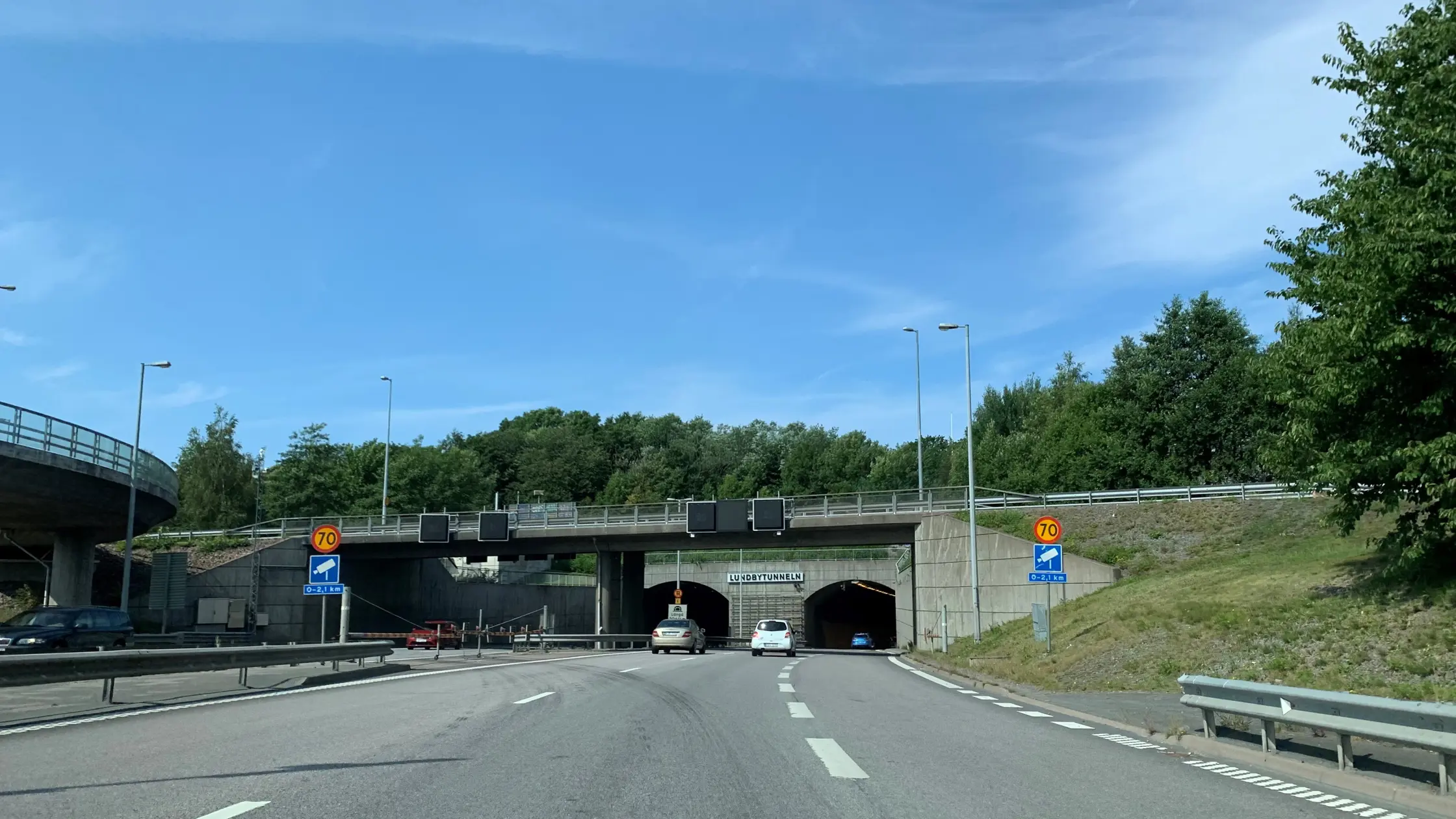Två bilar är påväg mot infarten till  Lundbytunneln strax  under bron vid Eriksbergsmotet en solig julidag.