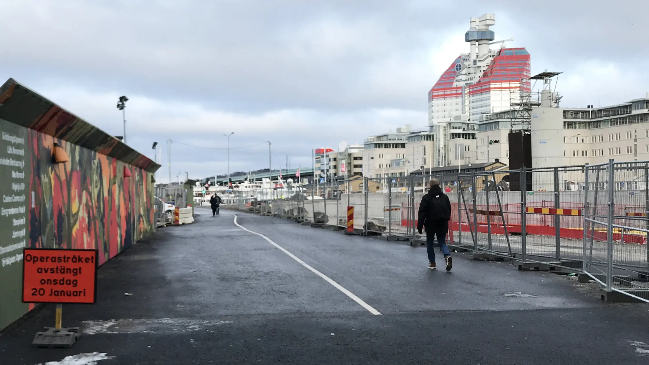 Två gående på gång- och cykelvägen mellan Operagatan och Sankt Eriksgatan, även kallad "Operastråket". I förgrunden en infoskylt om avstängningen.