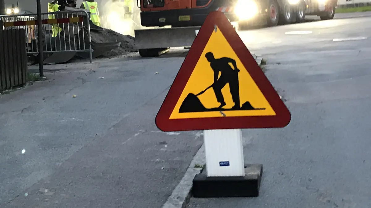 Vägarbetesskylt med maskin i bakgrunden.